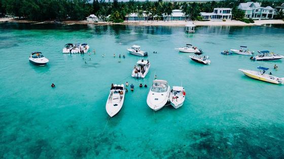 Image of a group of boats docked at a sandbar, with swimmers in the water.